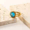 Detail of 18K gold-plated ring featuring a large blue zircon on a beige stone slab - US 10 / Gold Aqua Blue Zirconia