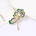 Elegante broche de pavo real dorado con esmalte azul y detalle de perla blanca - Flor de Pluma de Pavo Real