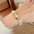 Elegante Vintage-Golduhr mit Doppelstrang-Perlenarmband am Handgelenk einer Frau - Goldgehäuse Goldfarbenes Zifferblatt