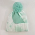 Détail d'un bonnet en maille tie-dye avec un grand pompon en fourrure et bord côte élastique - vert clair