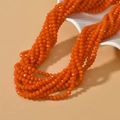 Orange faceted glass rondelle bead necklace displayed on a white wavy ceramic jewelry tray - Orange Red
