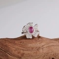 Macro detail of silver flower ring featuring pink gemstones on natural wood background - Silver Natural Ruby