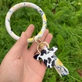 Détail du bracelet porte-clés en cuir PU avec charm de vache et pompon sur de l'herbe - Feuilles
