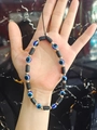Beaded phone strap with black discs, gold beads, and blue evil eye charm held by hand - Evil Eye Black