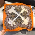 Detail shot of orange paisley print silk scarf on a plush rug and magazine - 70*70cm / Vibrant Orange Border Paisley