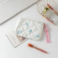 Close-up of quilted floral cosmetic bag with blue bow pattern and pink drawstring on a desk - White Background Blue Bow