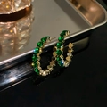 Dettaglio macro di orecchini a cerchio a C dorati con zirconi verdi scintillanti - Ago D'argento - Strass Rotondo Verde