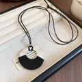 Detailed close-up of a geometric round pendant with hammered silver metal and black wood - Silver-Black