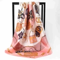 Detail of silk scarf showing pink and white fabric with gold chain and bag patterns - Pink