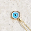 Golden evil eye pendant necklace with blue resin iris on a natural stone background - White Blue Eye