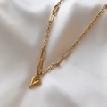 Detailed view of a gold heart pendant on a unique link chain over white silk fabric - Necklace / Gold