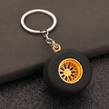 Miniature car tire keychain with black rubber and gold rim on leather surface - Imitation Gold