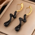 Primer plano de pendientes esmaltados en negro y dorado sobre caja de seda fina - Dorado Negro