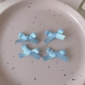 Dettaglio di quattro fiocchi in nastro di raso azzurro su un vassoio rosa a pois bianco - Blu