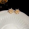 Macro de boucles d'oreilles fleurs dorées avec œil de chat et zircons sur plat blanc - Forme de Fleur Tridimensionnelle / Or
