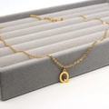 Close-up of golden letter Q pendant on a delicate chain in a velvet jewelry display tray - Letter Q / Gold