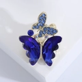 Dettaglio macro di spilla a farfalla dorata con cristalli blu scuro su sfondo bianco - Blu