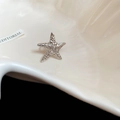 Elegant silver metal starfish ear clip earring presented on a minimalist white shell dish - Spiral Sea Star / Silver