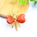 Detail of golden butterfly ornament with heart-shaped red natural stones on a wood tray - White K Plated Red Jasper