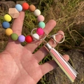 Detail of colorful silicone beaded bracelet keychain with leather tassel in hand - Rainbow