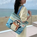 Blue canvas tote bag with cute penguin illustration and dark blue handles on a beach - Happy Penguin