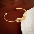 Makroaufnahme des vergoldeten Knoten-Armreifs mit Zirkon-Besatz auf Samthintergrund - Goldene Schleife Offenes Armband
