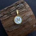 Golden round natural shell pendant featuring letter M on rustic wood texture - Letter M / 17x20mm