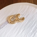 Primer plano detallado de pendientes de aro dorados en forma de C sobre plato cerámico - Pasador de Acero Dorado - Forma de C Redondeada (Diámetro 2,9 cm)