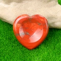 Polished red heart worry stone with natural dark veins placed on a green grass background - Red Jasper