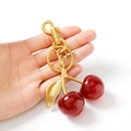 Porte-clés cerise rouge scintillant avec fermoir doré tenu en main sur fond blanc épuré - Cerise Rouge
