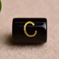 Macro shot of a black cylindrical bead featuring a gold foil engraved letter C design - Letter C