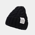 Close-up of black cable knit beanie texture with a white rectangular industrial patch - Black