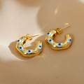 Detail shot of golden C-shaped hoop earrings with blue evil eye motifs and sparkling stones - Blue Evil Eye / Gold