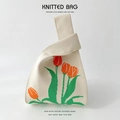 Close-up of cream knitted wrist bag featuring bright orange tulip and green leaf pattern - Beige Daffodil