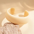 Minimalist thick open bangle in cream white acrylic on a natural stone display - White