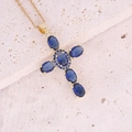 Dettaglio di un ciondolo a croce dorata con zirconi blu su una superficie di pietra - Blu Reale