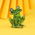 Green acrylic frog brooch with gold outlines and rhinestone eyes on a pleated backdrop - Green Cartoon Frog
