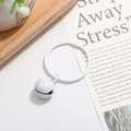 Close-up of white painted metal ring and bell keychain on minimalist white desk - White