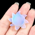 Carved iridescent lavender sun-shaped gemstone pendant held against black background - Opal (Synthetic)