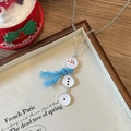 Détail d'un collier pendentif bonhomme de neige avec pompons bleus sur un plateau - Chaîne Argentée Écharpe Bleue Style Bonhomme de Neige