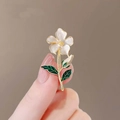 Elegant white floral brooch with gold stems and green leaves held in hand - Gardenia