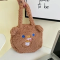 Detalle de un bolso de oso de peluche marrón con bordados y asas superiores firmes - café