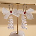 Detalle de pendientes con lazo de gasa, borlas de perlas, pedrería y piedras rojas en soporte - Blanco