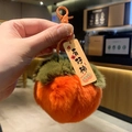 Close-up of plush persimmon keychain with orange fabric and Good Luck tag detail - Persimmon Good Things Happen