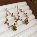 Close-up of handmade gold wire-wrapped earrings with red and bronze beads on velvet tray - Water Drop Beaded Style