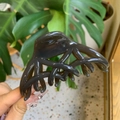 Dettaglio di una grande molletta per capelli in resina grigio scuro traslucida tenuta con mano - Coda di Fenice a Farfalla / grigio scuro