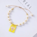 Detail of handmade beaded bracelet with white pearls and a yellow heart charm - Yellow Background White Heart