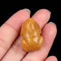 Hand-carved natural yellow jade frog crystal figurine held by hand on black background - Topaz