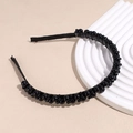 Detail view of a black beaded headband with woven glossy pearls on a white display stand - Black