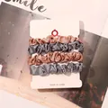Close-up of four satin scrunchies in gold and silver on a white display card - Champagne and Blue Gray